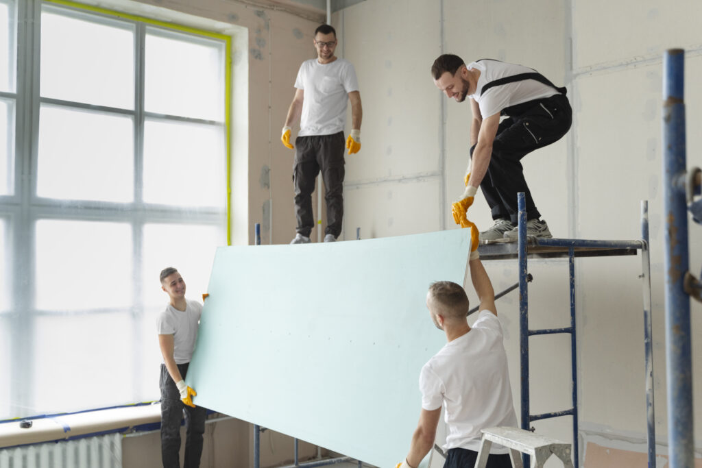 quatre plaquistes en train de monter une plaque de platre en hauteur - entreprise de renovation